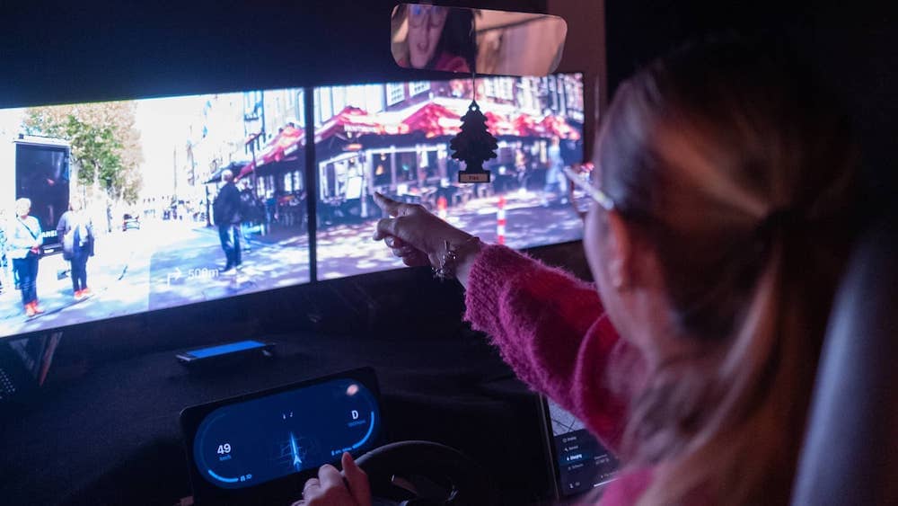 A student is pointing at pedestrians in a driving simulator